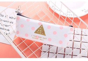 Pink polka dot canvas pencil case with zipper closure in a white metal storage basket