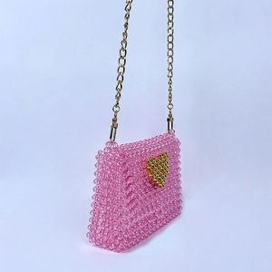 Close-up detail of a pink handmade beaded crossbody bag with a gold heart design.