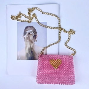 Detail of pink beaded mini bag featuring golden heart accent and metallic chain strap