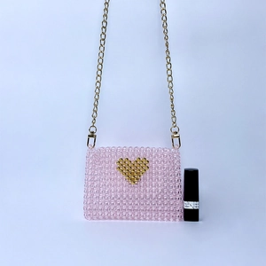 Detail of pink beaded handbag with gold heart pattern and metal chain strap