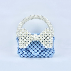 Dettaglio di borsa fatta a mano con perline blu e un grande fiocco bianco tessuto