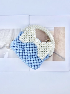 Borsa a mano fatta a mano con perle blu e bianche e fiocco su una rivista aperta