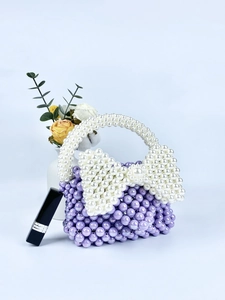 Dettaglio di una borsa in perle viola fatta a mano con un grande fiocco di perle bianche