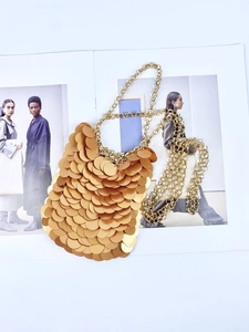 Detail of shimmering gold sequin chain bag laid on a fashion magazine background