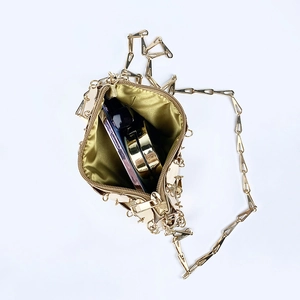 Borsa a tracolla dorata con catena metallica, aperta con telefono e trucco interno