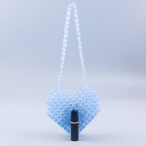 Close-up of handmade blue beaded heart bag showing acrylic texture and lipstick size scale