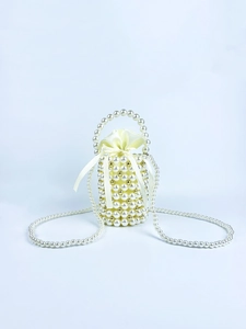 Detail of beaded bucket bag with white pearls, gold accents, and a satin drawstring bow