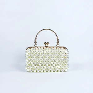 Detailed view of white faux pearls on evening bag with an ornate golden metal handle