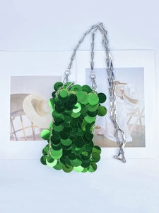 Close-up of emerald green sequin bag with silver chain on fashion magazine background