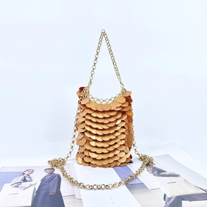Stylish gold sequin bucket bag with metal chain strap on fashion magazine backdrop