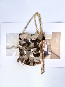Detailed view of shimmering gold paillette chain bag on a fashion magazine background