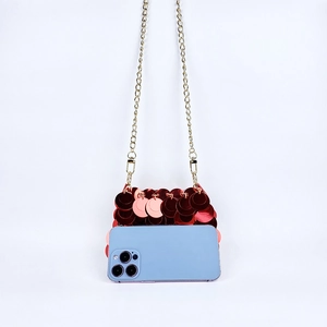 Détail d'un sac de soirée à paillettes rouges avec chaîne dorée à côté d'un smartphone