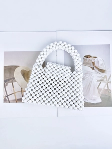 Detail of hand-woven white beaded handbag with acrylic beads on art magazine background