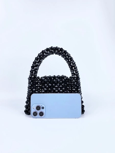 Detail shot of black beaded handbag next to a smartphone showing its spacious capacity