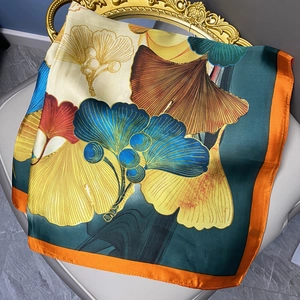 Ginkgo leaf print satin square scarf with orange borders on a decorative chair