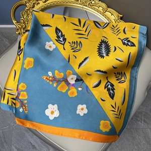 Silk-like satin square scarf with yellow and blue floral patterns on a leather chair