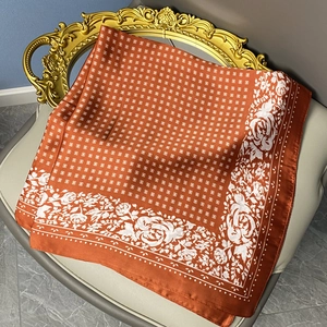 Detailed close-up of floral print silk scarf with white roses on orange fabric