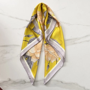 Detail of yellow silk scarf with rose floral prints and purple rolled edges on marble