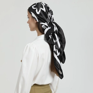 Détail d'un foulard carré en satin noir et blanc avec imprimé floral porté en turban