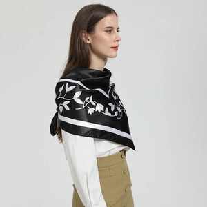 Elegant black silk scarf with white leaf patterns and satin finish shown on a female model