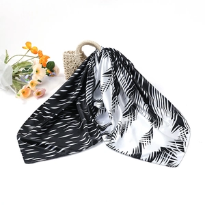 Gros plan d'un foulard en soie à motif feuilles de palmier noir et blanc sur un sac de plage