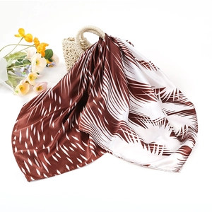 Carré de soie satiné marron et blanc avec motif plumes sur un sac de plage tissé