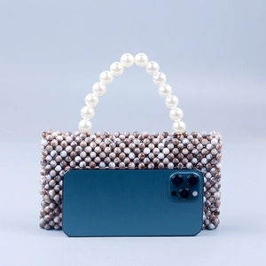Handmade marble-beaded bag with pearl handle compared to a smartphone for size scale