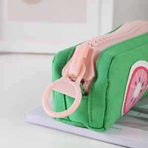 Close-up of a green canvas pencil case featuring a chunky pink zipper and fruit patch