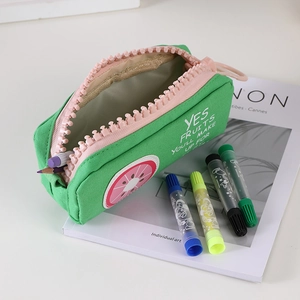 Green canvas pencil case with large pink zipper and fruit print shown on a magazine