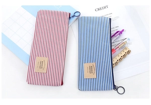 Close-up of striped canvas pencil cases with circular metal zippers and leather patches