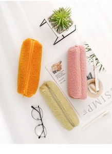 Detailed macro of soft plush pencil cases in orange, green, and pink with zippers