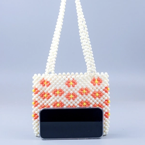 Detail of beaded mini bag with floral patterns shown next to a phone for size scale