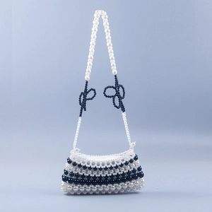 Handmade black and white pearl woven crossbody bag with bow accents on light blue background