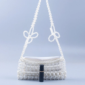 Handmade white pearl beaded handbag with floral weave and ribbon bows on blue backdrop