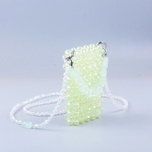 Detail showing hand-woven light green beaded crossbody bag with heart charm and metal clasp