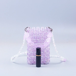 Detail of purple handmade beaded mini crossbody bag with heart charm and lipstick for scale