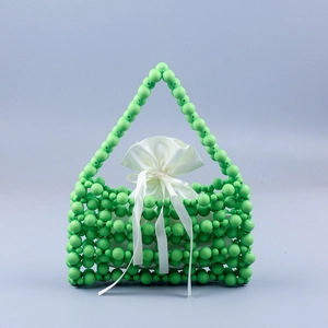 Detail of green beaded handbag with woven texture and a white satin drawstring pouch
