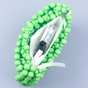 Detail view of handmade green beaded handbag interior holding lipstick and earphones