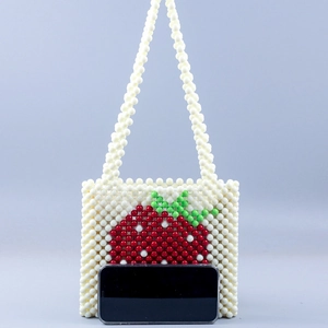 Handmade beaded strawberry shoulder bag with pearl-like beads and a smartphone for scale