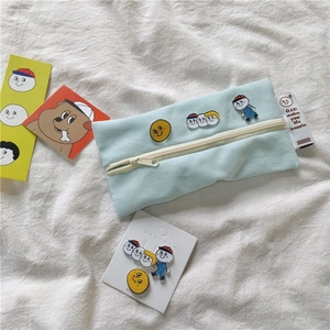 Detail of light blue canvas pencil case with cute cartoon pins on white fabric