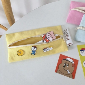 Detail of yellow canvas stationery bag with cute cartoon pins and zipper strap
