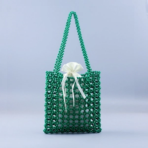 Detail of dark green beaded handbag featuring hollow mesh weave and white satin drawstring pouch