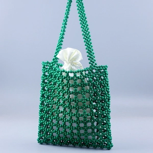 Detail of dark green beaded tote bag featuring hollowed-out floral patterns and satin liner