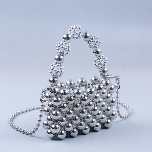 Detail of silver metallic beaded handbag with intricate flower-shaped woven handle detail