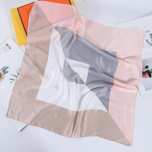 Flat lay of geometric color block silk scarf with pink and grey patterns on a gift box