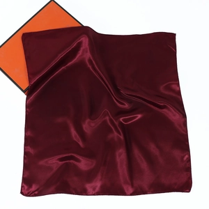Detail of burgundy satin silk square scarf with fine stitched edges near a gift box
