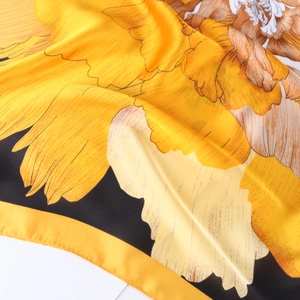 Detailed view of large orange peony print on silk scarf with elegant black borders
