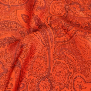 Detailed macro view of smooth orange paisley silk scarf with elegant floral patterns