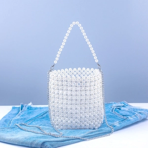 White acrylic pearl beaded bucket bag with silver chain strap on denim background