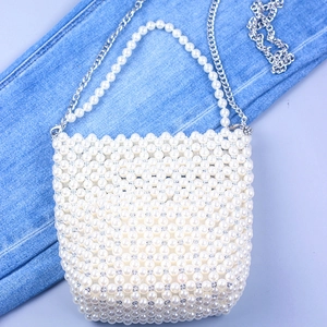 Detail of white handmade pearl beaded bucket bag with silver metal chain on denim background